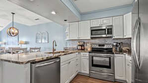 A modern kitchen with white cabinets, stainless steel appliances, a granite countertop, and a wooden floor. - Beautiful, dog-friendly w/amazing ocean views (North Myrtle Beach)