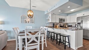 A modern kitchen with white cabinetry, a central island with bar stools, and a dining area with white chairs. - Beautiful, dog-friendly w/amazing ocean views (North Myrtle Beach)