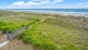 A beach with a wooden staircase leading down to the shore, surrounded by green vegetation. - Beautiful, dog-friendly w/amazing ocean views (North Myrtle Beach)