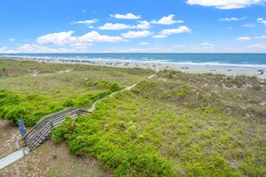 Een strand met een houten trap die naar het strand leidt, omringd door groene begroeiing.