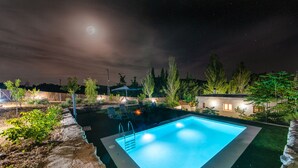 A rectangular swimming pool with a ladder, surrounded by a landscaped garden with various plants and trees. - Alpujarra Arena (Soportujar)