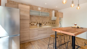 A modern kitchen with a stainless steel refrigerator, wooden cabinets, a wooden countertop, and a bar area with stools. - Alpujarra Arena (Soportujar)