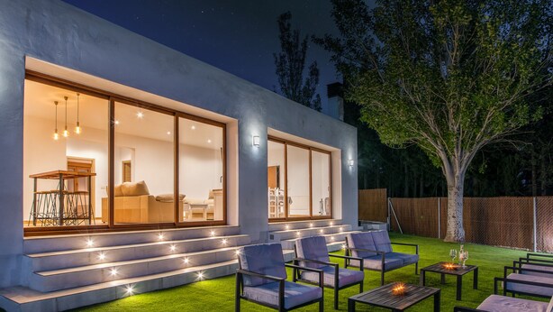 A modern house with large glass windows, outdoor seating, and a well-lit staircase. - Alpujarra Arena (Soportujar)