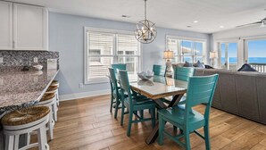 A modern kitchen with a dining area, wooden flooring, and large windows.