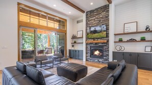 A modern living room with a fireplace, leather sofas, and a dining area with a view of the outdoors. - Golf View, Hot Tub, Suncadia Pool Access (Cle Elum)