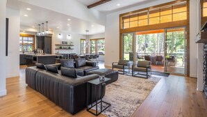 A spacious living area with a large sectional sofa, a kitchen in the background, and a view of the outdoors through large windows. - Golf View, Hot Tub, Suncadia Pool Access (Cle Elum)