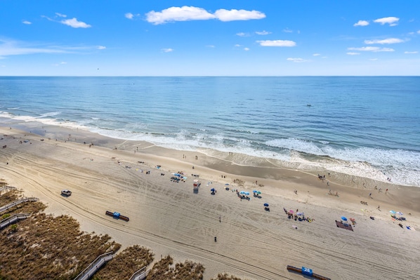 Una playa extensa con cielo despejado, una torreta de salvavidas y algunas sombrillas.