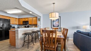 A modern kitchen with wooden cabinets, a black refrigerator, and a dining area with a wooden table and chairs. - Enjoy direct access to your private oceanfront balcony (North Myrtle Beach)