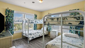 Una habitación con literas, un ventilador, una cesta de mimbre y una ventana con cortinas.