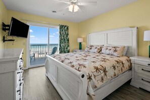A bedroom with a bed, a TV, a balcony with a view of the beach, and a ceiling fan. - Oceanfront duplex steps from beach w/shared pool, game room, kids' pool, grill (North Myrtle Beach)