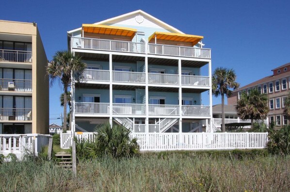 A multi-story hotel with balconies, a white fence, and palm trees.