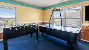 Una habitación con mesa de futbolín y mesa de billar, ventanas amplias con persianas y vistas al exterior.