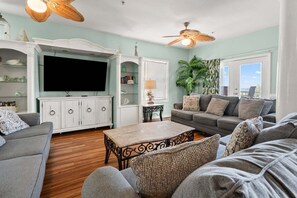 A living room with a television, white cabinets, a sofa, a coffee table, and a ceiling fan. - Oceanfront duplex steps from beach w/shared pool, game room, kids' pool, grill (North Myrtle Beach)