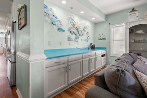 A kitchen with white cabinets, a blue countertop, and decorative wall art. - Oceanfront duplex steps from beach w/shared pool, game room, kids' pool, grill (North Myrtle Beach)