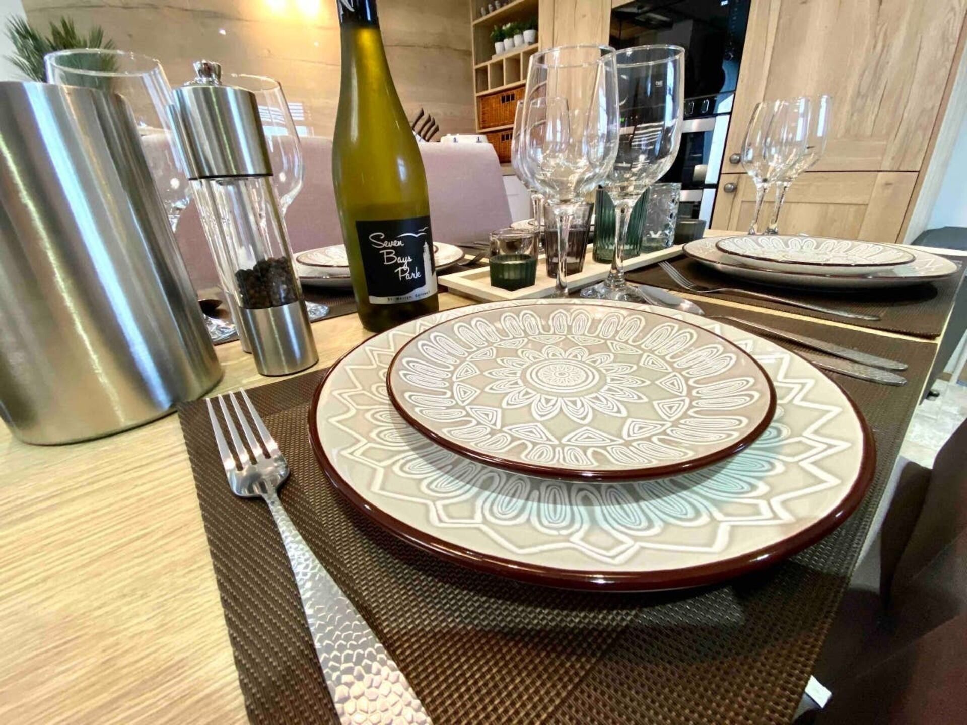 Taula de menjador preparada amb un plat decoratiu, una ampolla de vi i diversos vasos.