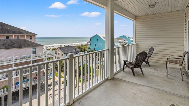 Een balkon met uitzicht op het strand en de oceaan, twee Adirondack stoelen en een witte balustrade.