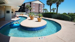 A pool area with a 3 FT no diving sign, palm trees, and a building in the background. - Luxury oceanfront resort-workout room, indoor/outdoor pools, lazy river, kids' pool-in Ocean Drive (North Myrtle Beach)