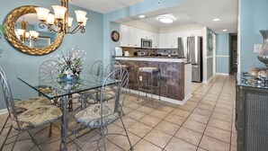 A modern kitchen with a central island, stainless steel appliances, and a dining area with a glass table and metal chairs. - Luxury oceanfront resort-workout room, indoor/outdoor pools, lazy river, kids' pool-in Ocean Drive (North Myrtle Beach)