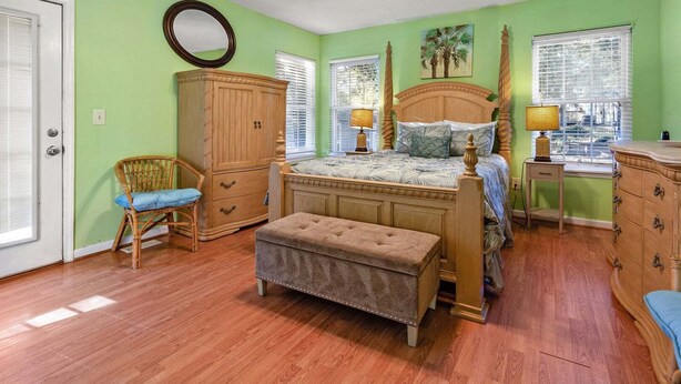 A bedroom with a bed, a wooden wardrobe, a bench, a chair, and a window with blinds.