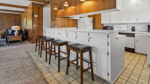 Een keuken met houten kastjes, een wit aanrecht en barstoelen.
