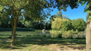 A serene lakeside setting with a tent and a boat on the water, surrounded by lush greenery and trees. - Chalet du Moulin des fontaines near the Pont du Gard (Saint-Paul-les-Fonts)