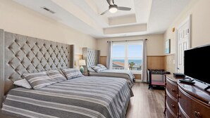 Une chambre avec deux lits, un ventilateur de plafond, une télévision et une vue sur la mer.