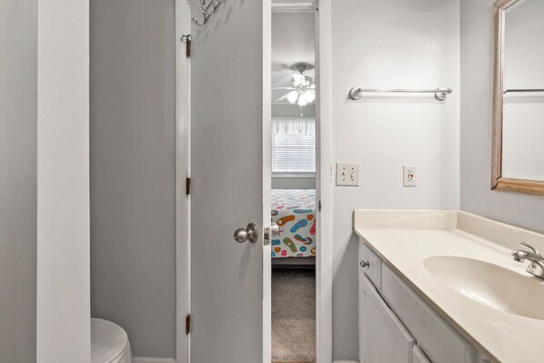 A bathroom with a toilet, a sink, a mirror, and a ceiling fan.