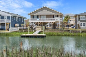 A waterfront property with a dock, a covered deck, and a two-story house with a balcony.