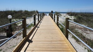 A wooden boardwalk leading to the beach with metal railings and a sandy path on either side. - Perfect setting for your getaway with stunning views (North Myrtle Beach)