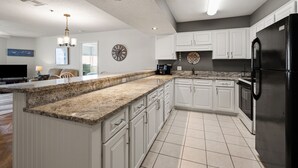 A modern kitchen with white cabinets, granite countertops, a black refrigerator, and a clock on the wall. - Perfect setting for your getaway with stunning views (North Myrtle Beach)