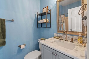 Een badkamer met een blauwe wand, een wit toilet, een wastafel met een marmeren aanrechtblad, een spiegel met een decoratieve lijst en een handdoekhouder.