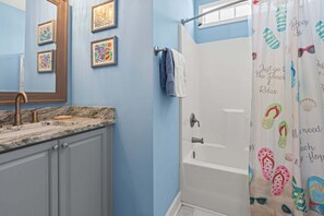 A bathroom with a sink, mirror, and shower curtain with beach-themed prints.