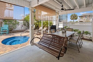 A covered patio with a pool, outdoor seating, and a view of neighboring houses.