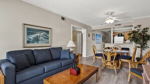 A living room with a blue sofa, wooden coffee table, wicker chairs, and a dining area with a white table and chairs. - Upscale family resort w/all the amenities-large pool, tennis courts, hot tub and more (North Myrtle Beach)