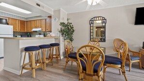 A modern kitchen with wooden cabinets, a bar area with stools, a dining table with chairs, and a large mirror on the wall. - Upscale family resort w/all the amenities-large pool, tennis courts, hot tub and more (North Myrtle Beach)