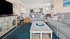 A modern living room with a grey sofa, a white coffee table, and a television on a cabinet. - Step into luxury at SEA POINTE 802, where your personal beachfront paradise awaits. (North Myrtle Beach)