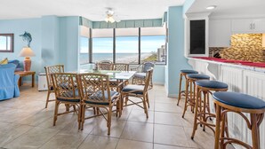 A dining area with a view of the beach, a kitchen with a tiled backsplash, and a bar area with stools.
