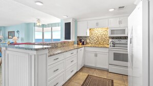 A kitchen with white cabinetry, a granite countertop, a stone backsplash, a microwave, an oven, and a window with a view.