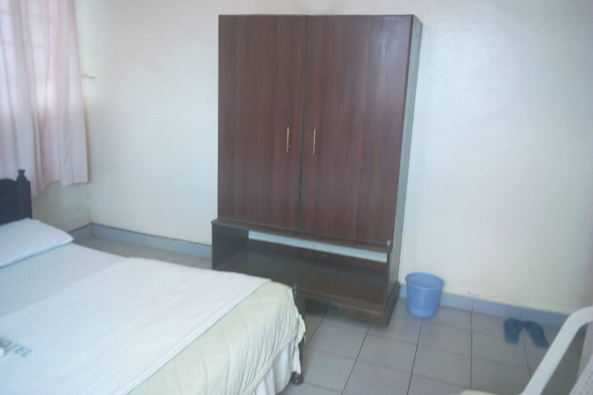 Un dormitorio con una cama, un armario, un cubo azul y una silla.