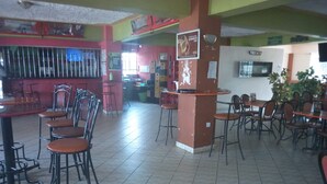 A restaurant interior with multiple tables and chairs, a counter, and a television screen. - Gempark Grand Hotel (Thika)