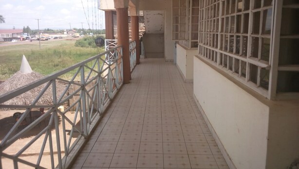 A corridor with tiled flooring, metal railings, and a view of a grassy area and vehicles in the distance. - Gempark Grand Hotel (Thika)