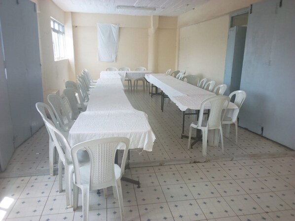 A conference room with a long table and chairs, tiled floor, and a plain wall with a window. - Gempark Grand Hotel (Thika)