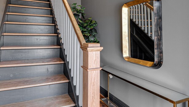A staircase with wooden steps and a wooden handrail, leading to a landing with a mirror and a plant. - Brand New, Gorgeous Studio Close to Everything! (Richmond)