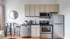 A modern kitchen with a microwave, oven, and refrigerator, a round mirror, and a dining area with stools. - Brand New, Gorgeous Studio Close to Everything! (Richmond)