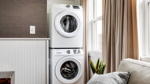 A stacked washer and dryer unit in a room with a window, curtains, and a plant. - Brand New, Gorgeous Studio Close to Everything! (Richmond)