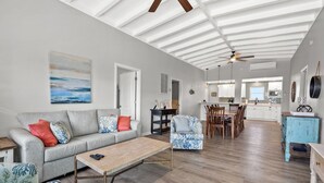 A spacious living room with a sofa, armchairs, and a coffee table. A dining area with chairs and a table is visible in the background. - Channel home w/gorgeous saltwater pool, relaxing porches-fish, swim, sunbathe, enjoy! (North Myrtle Beach)