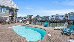 A swimming pool with a brick deck, surrounded by lounge chairs and a fence. - Channel home w/gorgeous saltwater pool, relaxing porches-fish, swim, sunbathe, enjoy! (North Myrtle Beach)