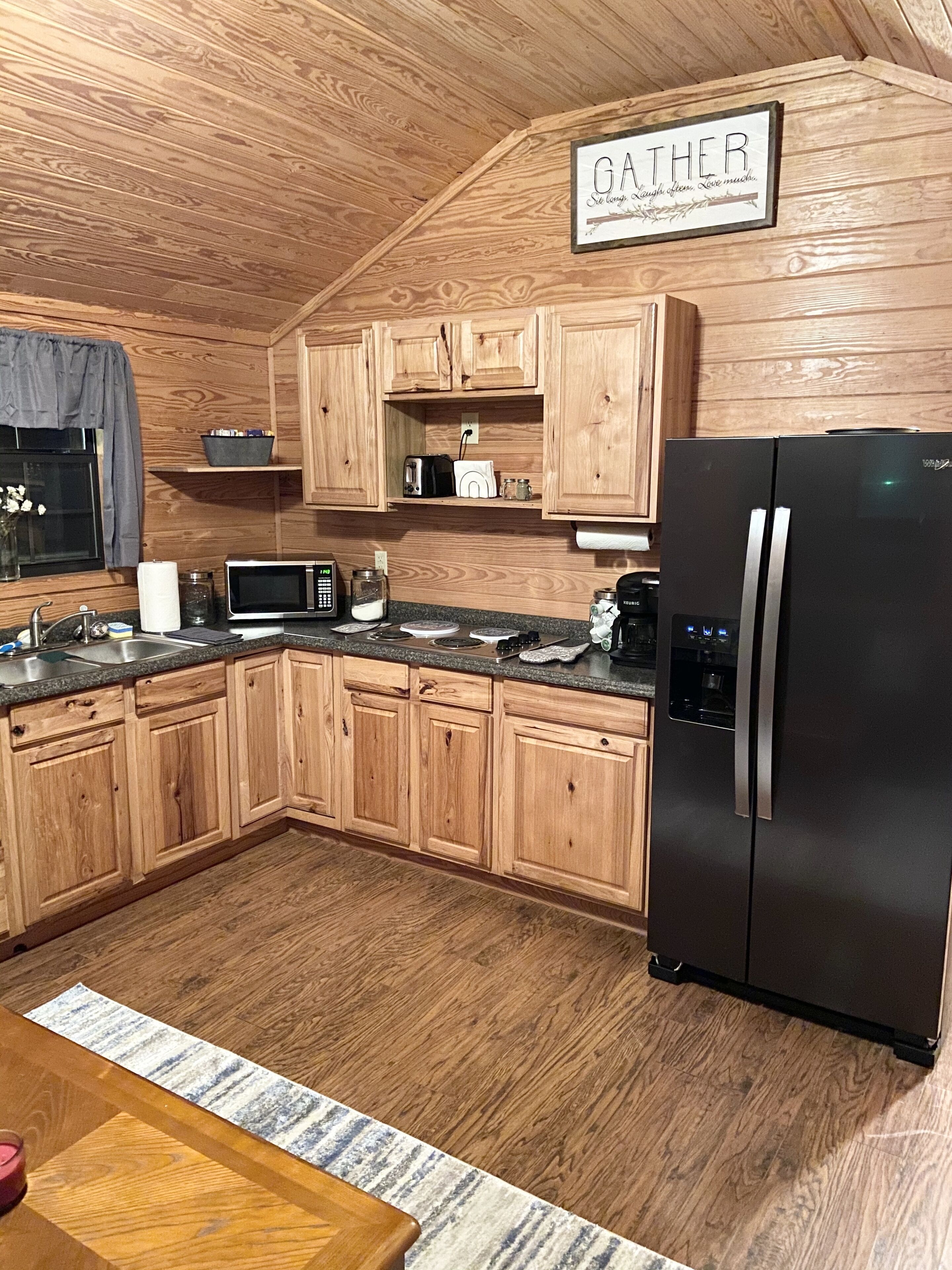 Une cuisine avec des meubles de rangement en bois, un réfrigérateur noir, un four à micro-ondes et un grille-pain.