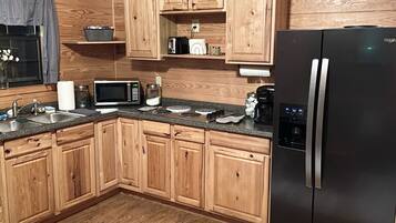Une cuisine avec des meubles de rangement en bois, un réfrigérateur noir, un four à micro-ondes et un grille-pain.