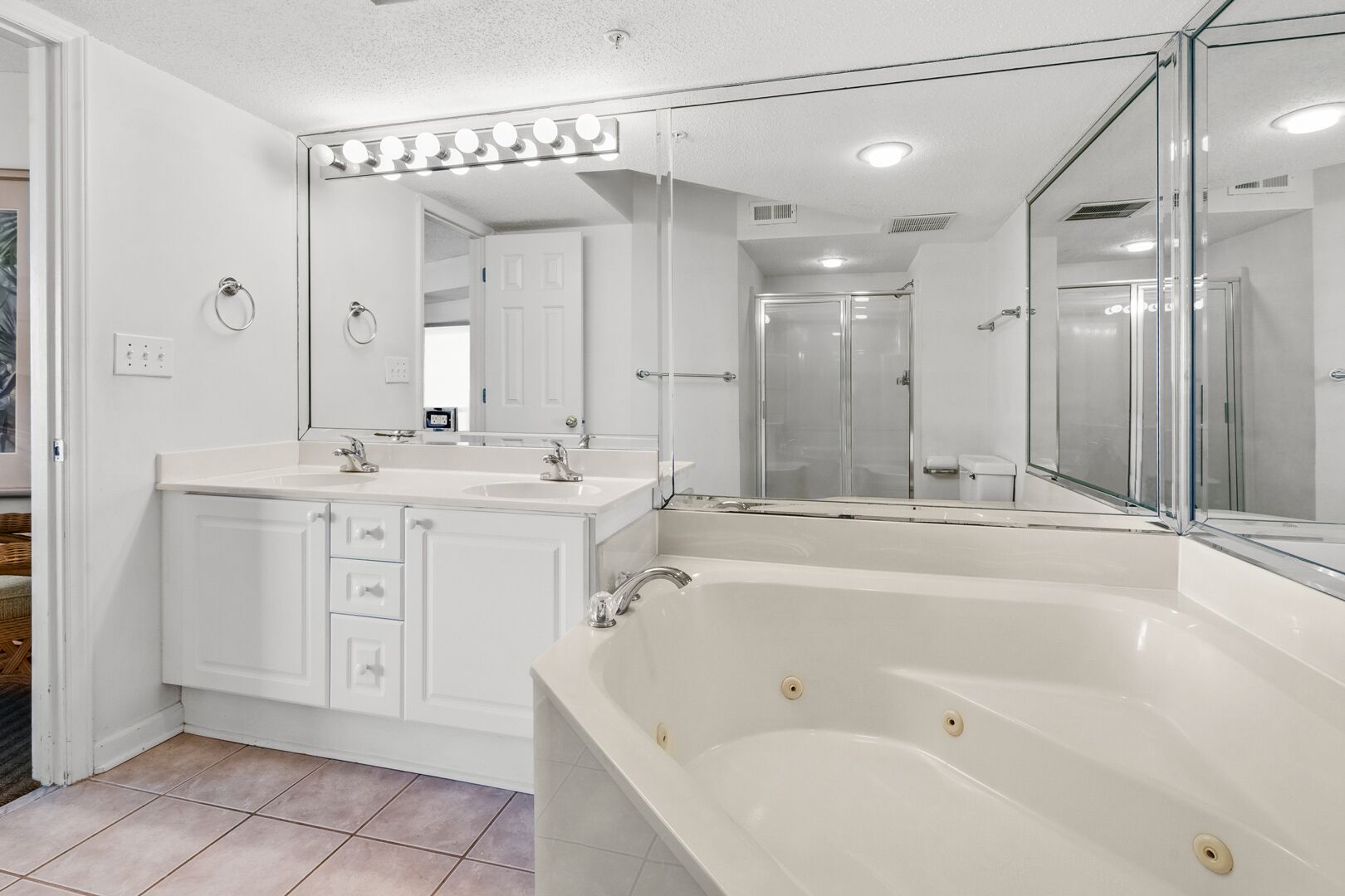 A modern bathroom with a large bathtub, a double sink vanity, and a mirror with lights above.